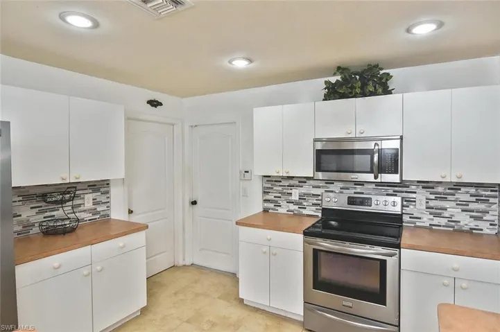 Kitchen with white cabinets, tasteful backsplash, light tile floors, and appliances with stainless steel finishes
