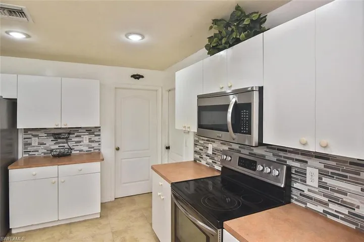 Kitchen featuring stainless steel appliances, butcher block counters, light tile flooring, backsplash, and white cabinets