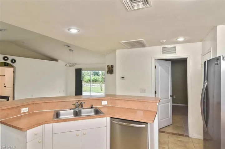 Kitchen with lofted ceiling, appliances with stainless steel finishes, white cabinets, sink, and light tile floors