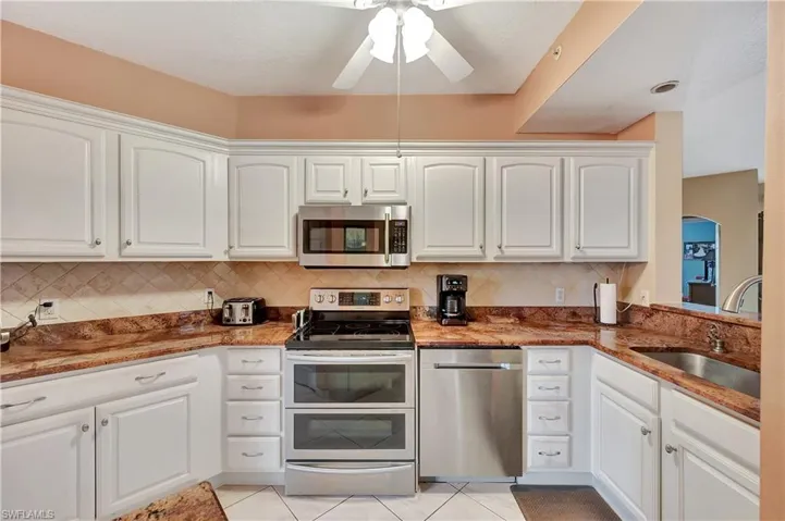 Kitchen with decorative backsplash, stainless steel appliances, white cabinets, and sink