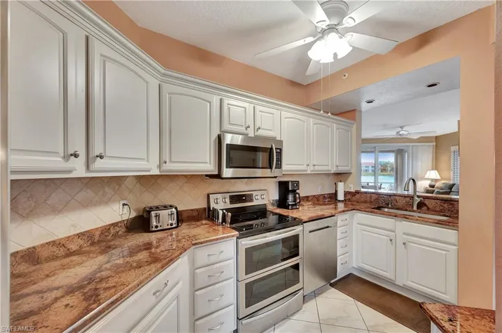 Kitchen featuring dark stone counters, sink, white cabinetry, stainless steel appliances, and ceiling fan