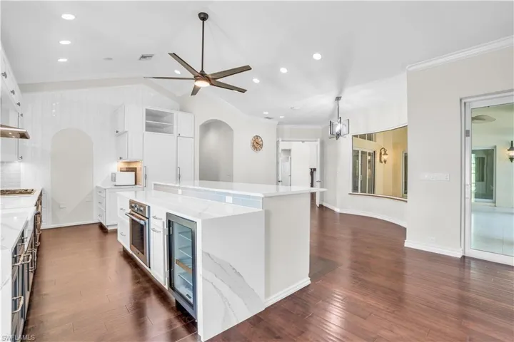 Kitchen with light stone counters, dark hardwood / wood-style flooring, a kitchen island, and wine cooler