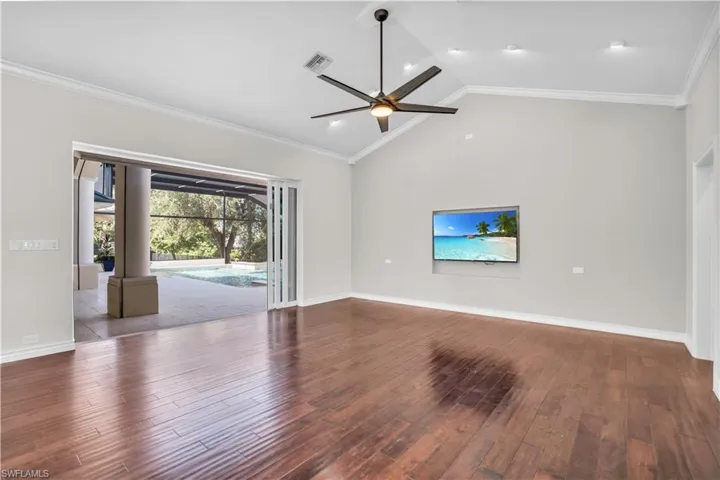 Living room with ceiling fan, ornamental molding, hardwood / wood-style floors, and high vaulted ceiling
