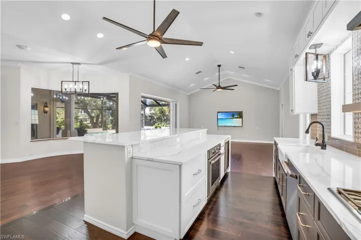 Kitchen with ornamental molding, light stone counters, dark hardwood / wood-style floors, vaulted ceiling, and white cabinets