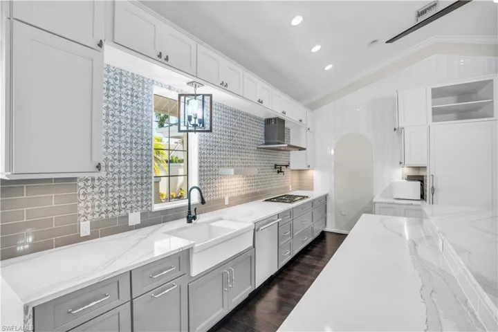 Kitchen with lofted ceiling, dark wood-type flooring, wall chimney range hood, and tasteful backsplash