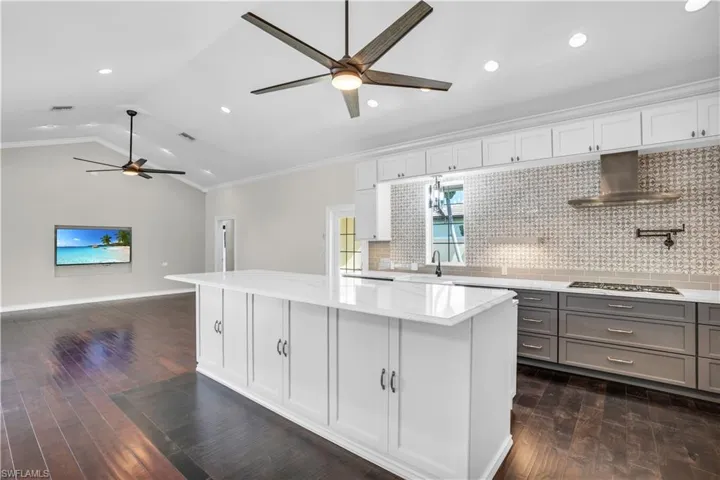 Kitchen with wall chimney exhaust hood, a kitchen island, dark hardwood / wood-style flooring, and ornamental molding