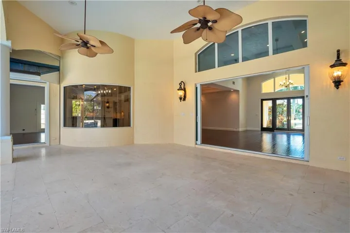 Tiled empty room with ceiling fan with notable chandelier, high vaulted ceiling, and french doors