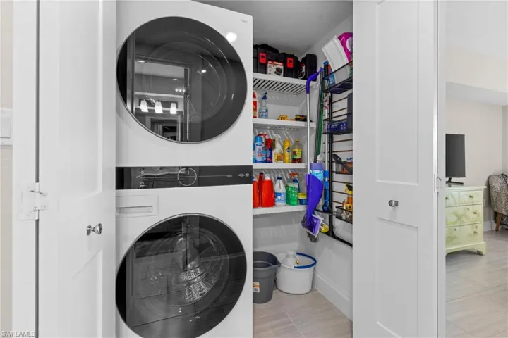 Utility closet featuring a stacked washer and dryer, white shelving, and tile flooring