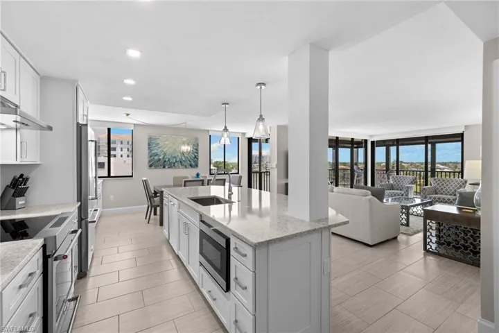 Open-concept kitchen featuring an island with an undermount sink, stainless steel appliances, light cabinetry, and light-toned tile flooring