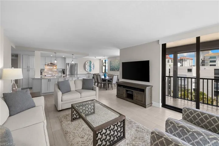 Open-concept living space featuring wood-finish flooring, a kitchen with light cabinetry and stainless steel appliances, a dining area, and a glass sliding door opening to a balcony with black railings