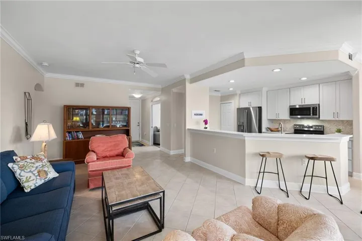 Living area with baseboards, visible vents, light tile patterned flooring, ceiling fan, and crown molding