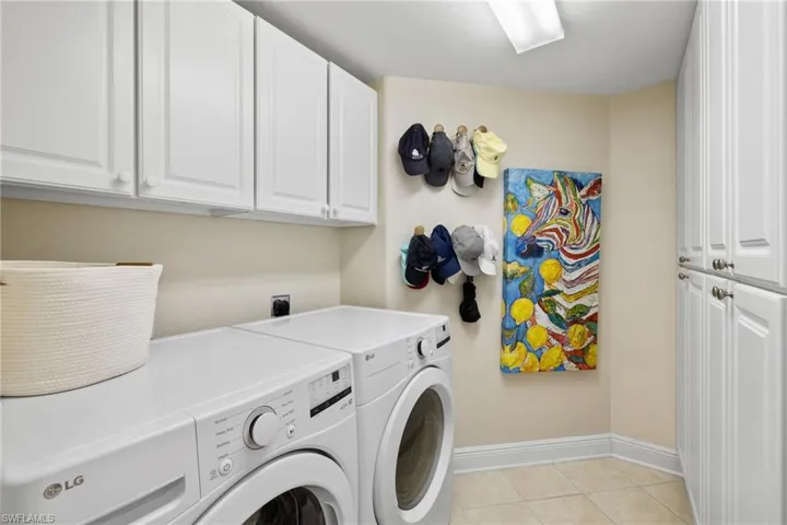 Laundry area featuring light tile patterned floors, cabinet space, washer and dryer, and baseboards