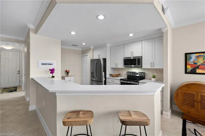 Kitchen with tasteful backsplash, a breakfast bar, ornamental molding, light tile patterned flooring, and stainless steel appliances