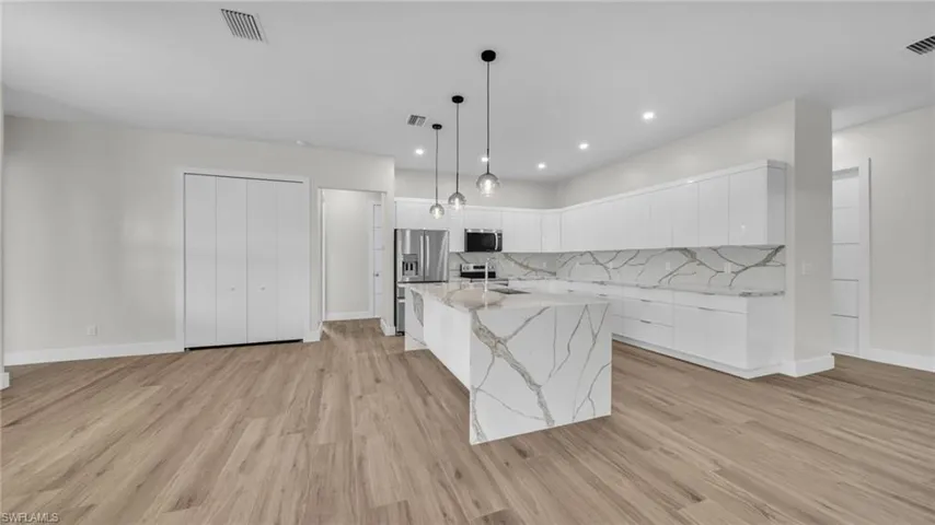Kitchen featuring white cabinets, modern cabinets, pendant lighting, light stone countertops, and decorative backsplash