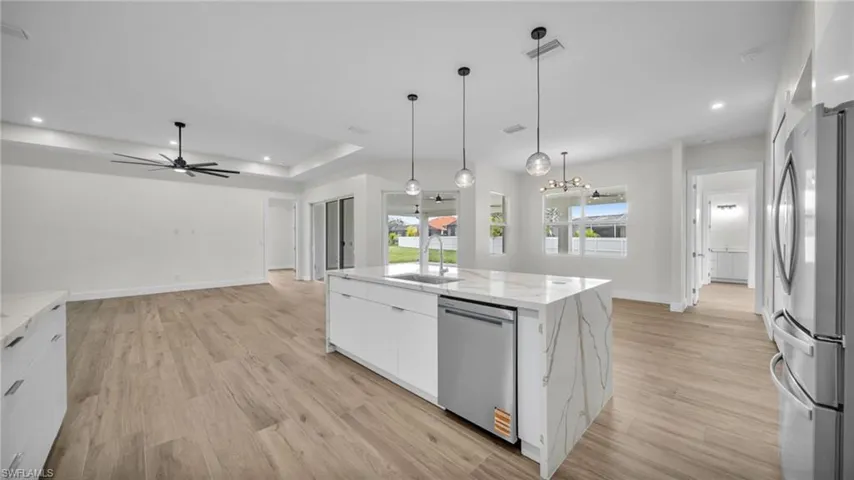 Kitchen with white cabinets, appliances with stainless steel finishes, light wood finished floors, decorative light fixtures, and light stone countertops