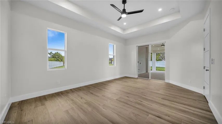 Unfurnished room with a raised ceiling, light wood-type flooring, a ceiling fan, and recessed lighting