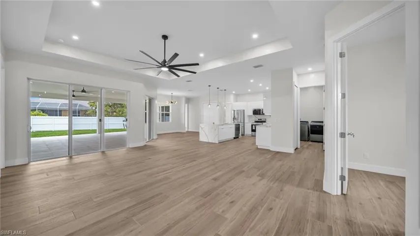Unfurnished living room featuring a raised ceiling, ceiling fan, light wood finished floors, a chandelier, and recessed lighting