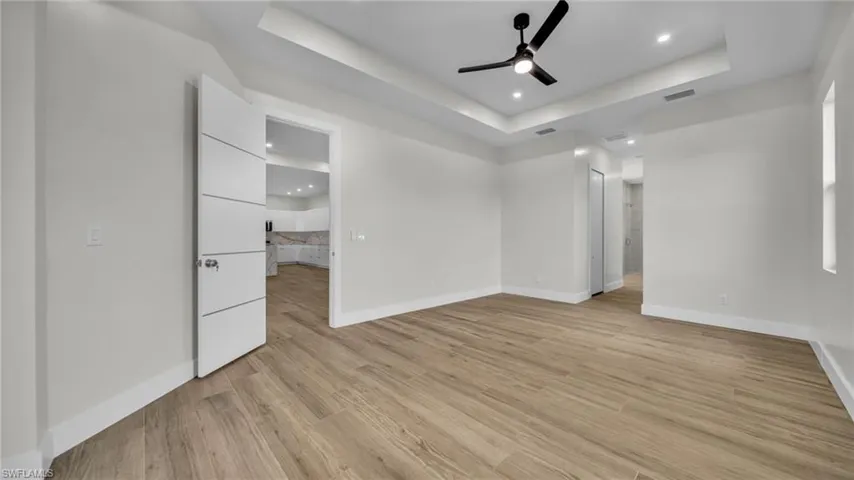 Unfurnished room featuring a tray ceiling, light wood-style flooring, recessed lighting, and ceiling fan