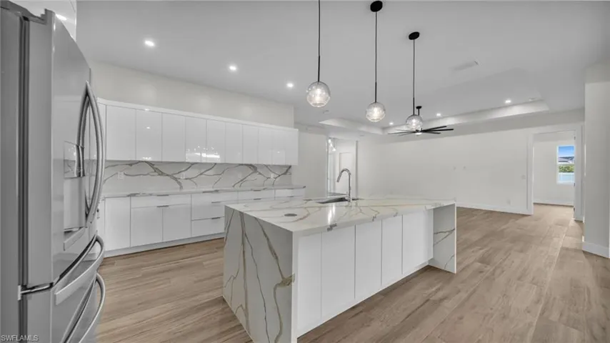 Kitchen with stainless steel refrigerator with ice dispenser, modern cabinets, white cabinets, light stone countertops, and backsplash