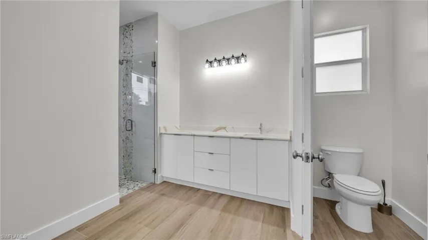 Full bath featuring a shower stall, double vanity, and light wood finished floors