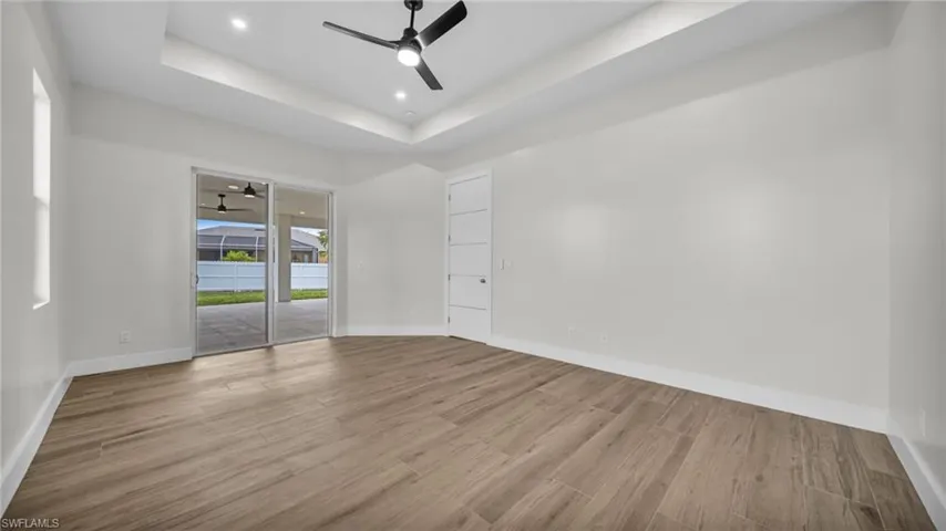 Unfurnished room featuring a raised ceiling, wood finished floors, a ceiling fan, and recessed lighting