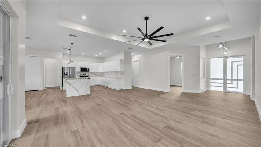 Unfurnished living room featuring a raised ceiling, recessed lighting, light wood-type flooring, and ceiling fan