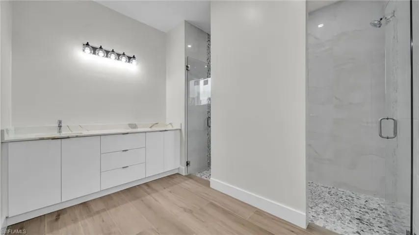 Full bathroom with a marble finish shower, double vanity, and light wood-type flooring