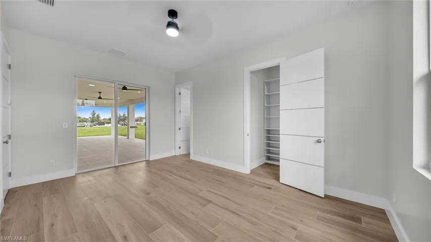 Unfurnished bedroom featuring access to exterior, light wood finished floors, a ceiling fan, and a spacious closet