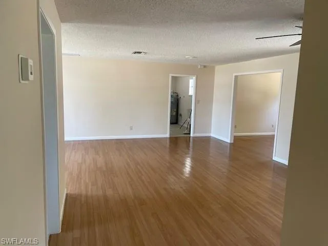 Spare room with wood finished floors, a textured ceiling, baseboards, strapped water heater, and ceiling fan