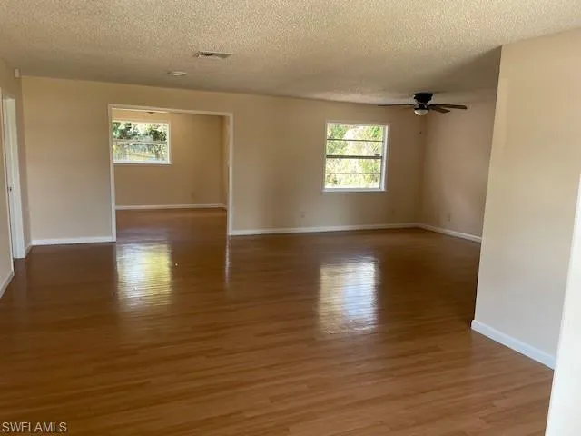Empty room with a ceiling fan, a textured ceiling, light wood-type flooring, and baseboards