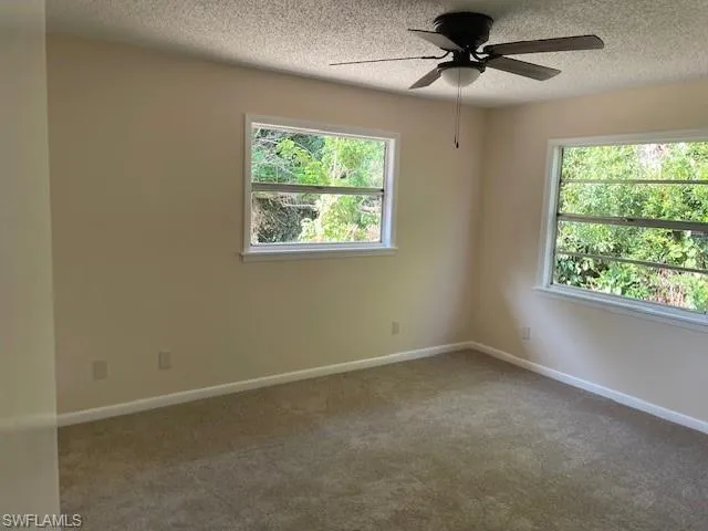 Carpeted empty room with a ceiling fan, healthy amount of natural light, a textured ceiling, and baseboards