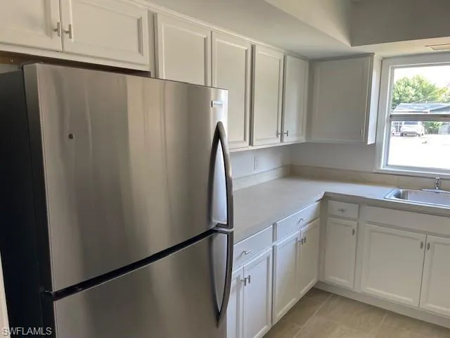 Kitchen featuring freestanding refrigerator, a sink, light countertops, and white cabinets