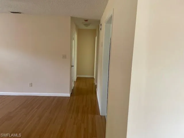 Hallway with wood finished floors, baseboards, and a textured ceiling
