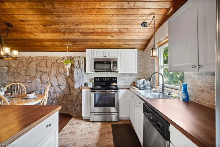 Kitchen featuring appliances with stainless steel finishes, white cabinetry, hanging light fixtures, and wood counters