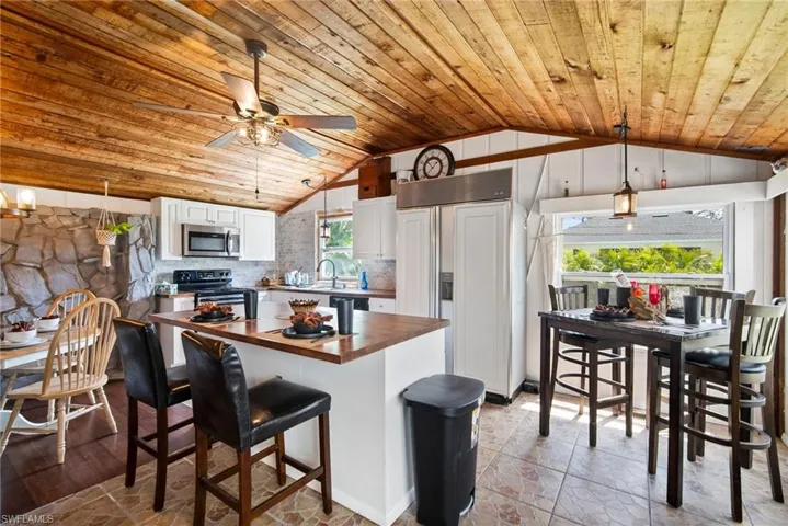 Kitchen with white cabinetry, hanging light fixtures, lofted ceiling, range with electric cooktop, and tasteful backsplash