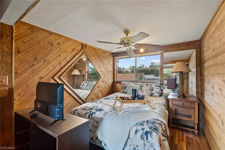 Bedroom with ceiling fan, wood walls, and wood-type flooring