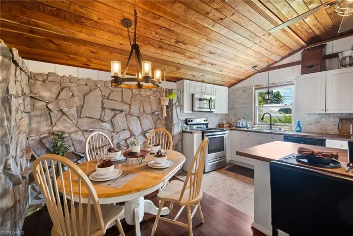 Dining space with vaulted ceiling, an inviting chandelier, light hardwood / wood-style floors, wooden ceiling, and sink