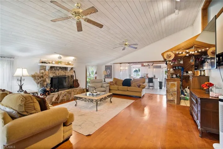 Living room with hardwood / wood-style floors, a stone fireplace, ceiling fan, and wood ceiling