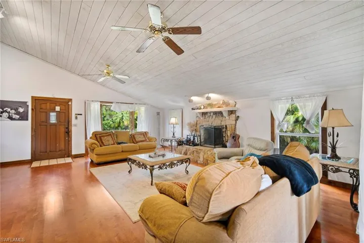 Living room with a stone fireplace, hardwood / wood-style floors, a wealth of natural light, and wood ceiling