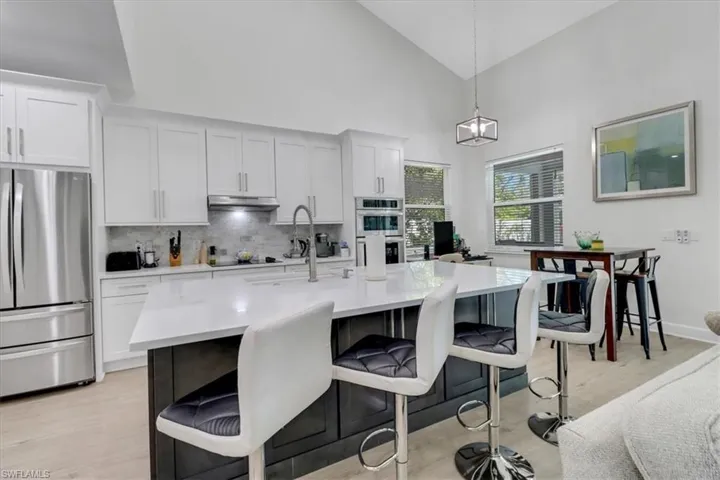 Kitchen featuring light wood-style flooring, a kitchen breakfast bar, backsplash, stainless steel appliances, and light countertops