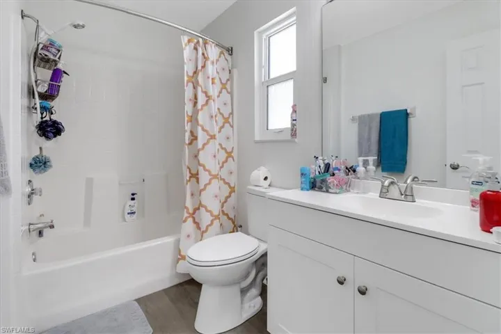 Full bath with vanity, shower / bath combination with curtain, toilet, and wood finished floors