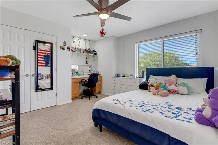 Bedroom with baseboards, light colored carpet, built in study area, and a ceiling fan