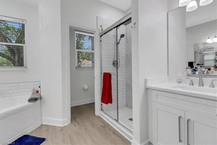 Bathroom with vanity, wood finished floors, baseboards, a stall shower, and a bath