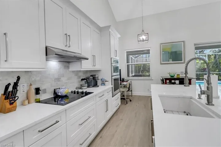 Kitchen featuring under cabinet range hood, a sink, white cabinetry, decorative backsplash, and black electric stovetop