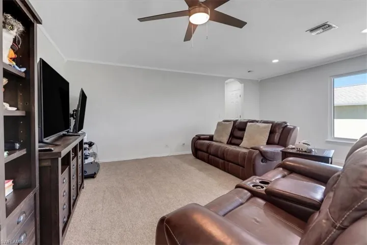 Living area with a ceiling fan, light colored carpet, visible vents, and ornamental molding