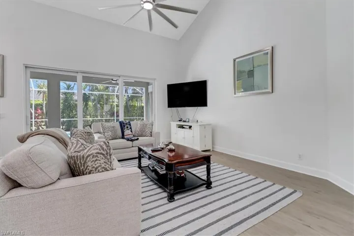 Living room featuring baseboards, high vaulted ceiling, wood finished floors, and a ceiling fan
