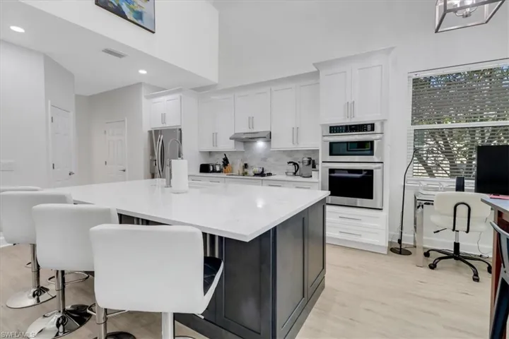 Kitchen featuring stainless steel appliances, decorative backsplash, light wood-style floors, under cabinet range hood, and white cabinetry