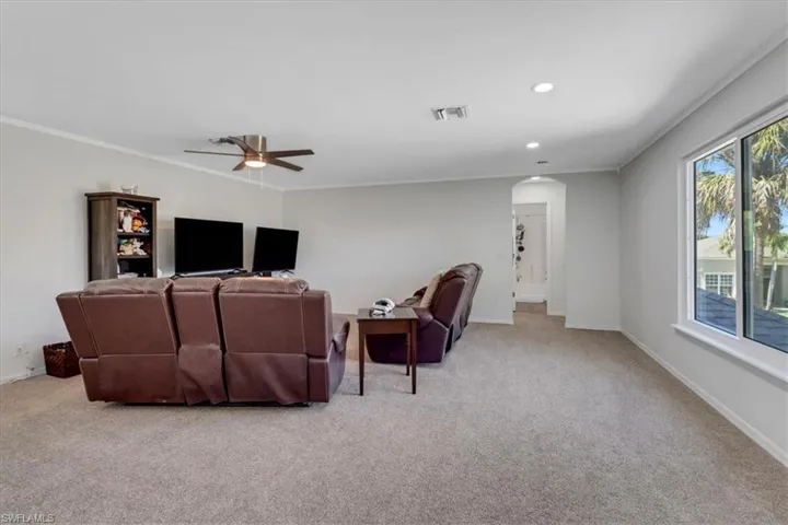 Carpeted living room featuring baseboards, visible vents, arched walkways, ceiling fan, and ornamental molding