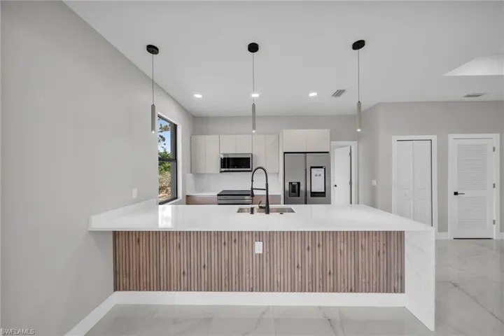 Kitchen featuring a peninsula, stainless steel appliances, modern cabinets, light stone countertops, and light marble finish floors