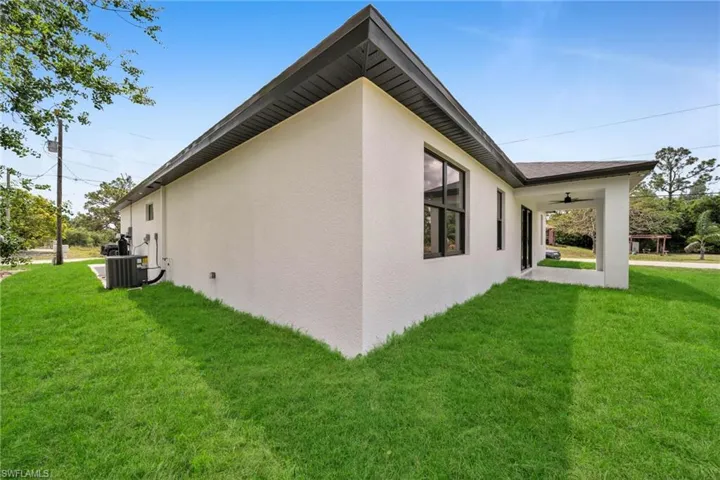 View of property exterior with a lawn, stucco siding, and a ceiling fan